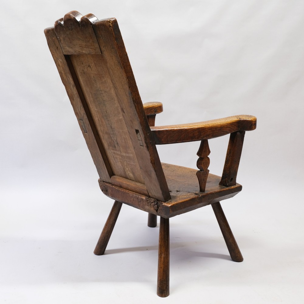 An antique mid-18th century dark oak panel-backed Windsor armchair featuring curved armrests, a shaped cresting rail, and splayed turned legs. View III