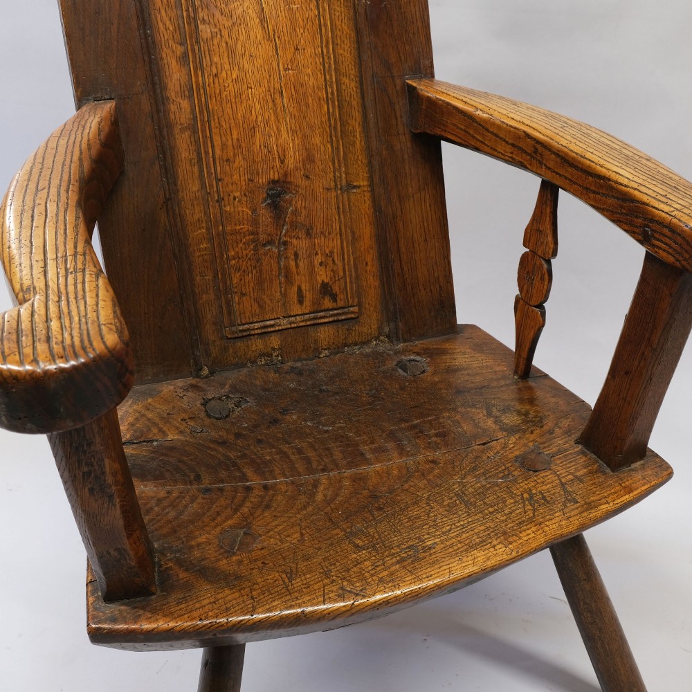 An antique mid-18th century dark oak panel-backed Windsor armchair featuring curved armrests, a shaped cresting rail, and splayed turned legs. View IV