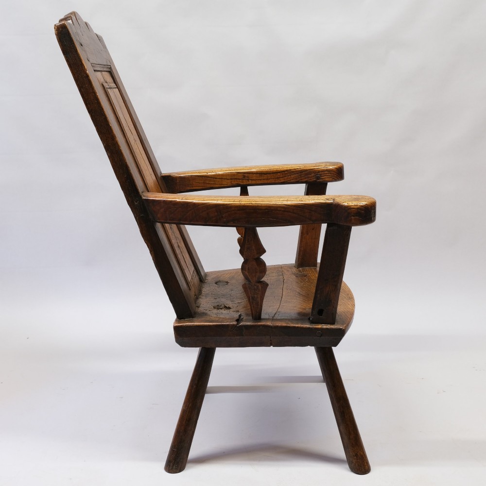 An antique mid-18th century dark oak panel-backed Windsor armchair featuring curved armrests, a shaped cresting rail, and splayed turned legs. View V