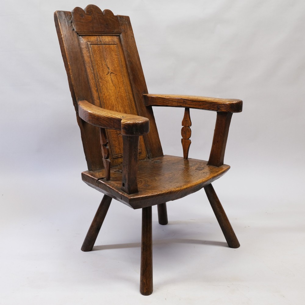 An antique mid-18th century dark oak panel-backed Windsor armchair featuring curved armrests, a shaped cresting rail, and splayed turned legs. View VI