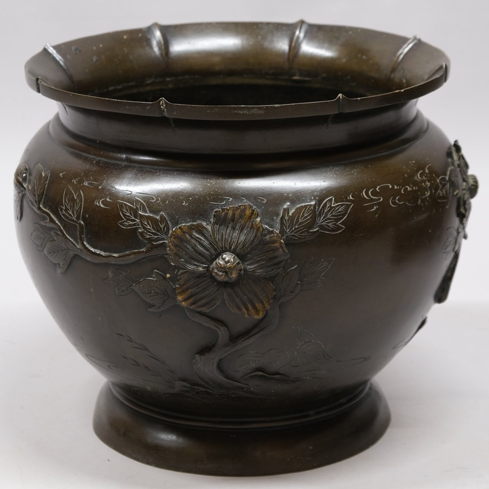 A dark bronze cast metal jardiniere featuring a scalloped rim, flared circular base, and raised floral relief decorations around the main body.