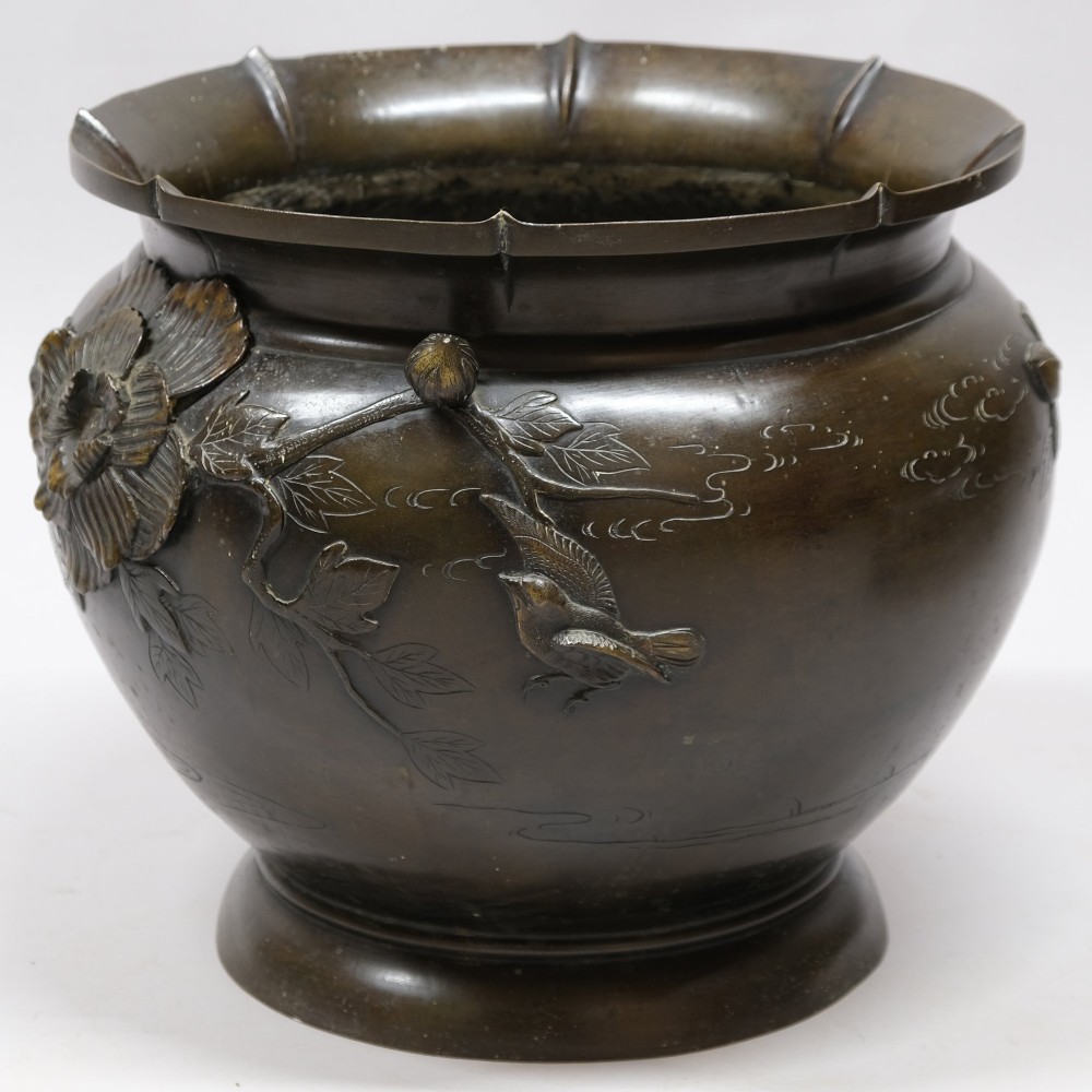 A dark bronze cast metal jardiniere featuring a scalloped rim, flared circular base, and raised floral relief decorations around the main body. View III