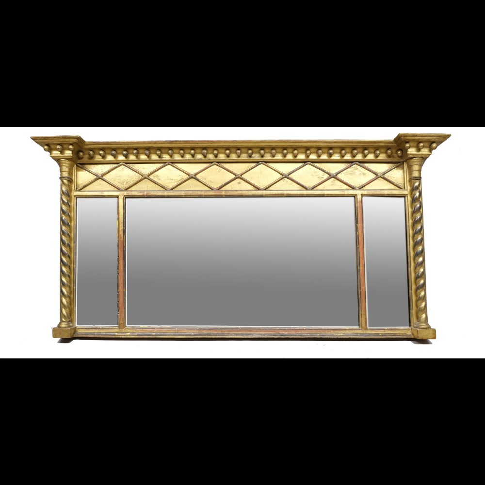 A broad horizontal Regency giltwood overmantel mirror featuring a triple-plate glass design, spherule ball cornice, diamond frieze, and flanking spiral-turned columns.
