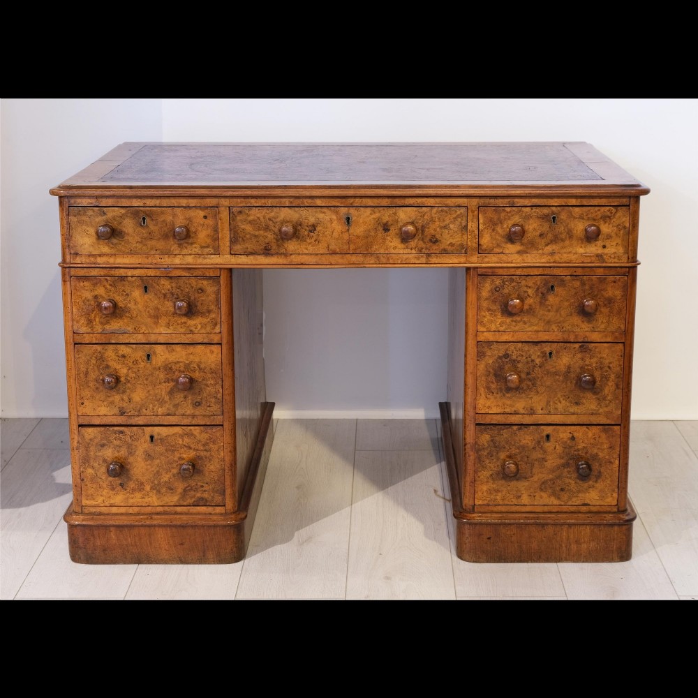 A Victorian burr walnut pedestal desk featuring nine drawers with turned wooden knobs and an inset leather writing surface.