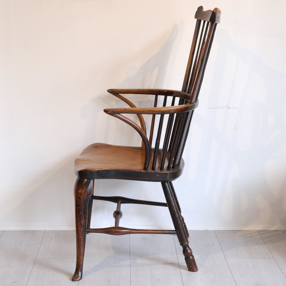 An 18th-century comb back Windsor armchair in warm brown timber, featuring a pierced central splat, spindle back, cabriole front legs, and a carved saddle seat. View III