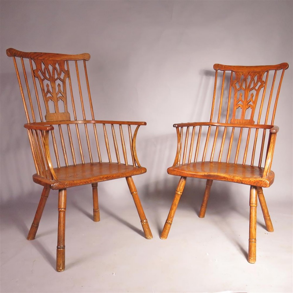 A pair of late eighteenth-century timber comb-back Windsor armchairs featuring pierced splats, slender spindles, saddled seats, and splayed turned legs.
