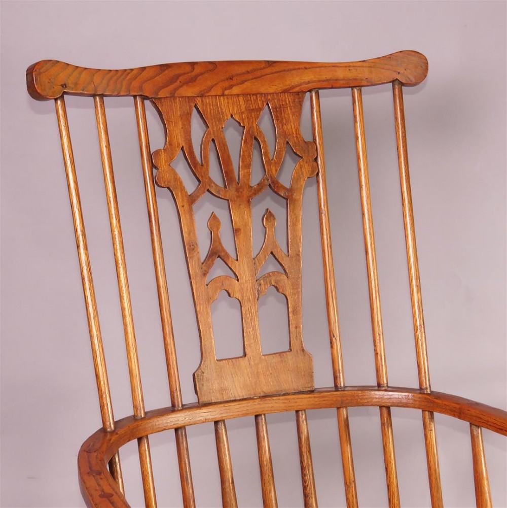 A pair of late eighteenth-century timber comb-back Windsor armchairs featuring pierced splats, slender spindles, saddled seats, and splayed turned legs. View II