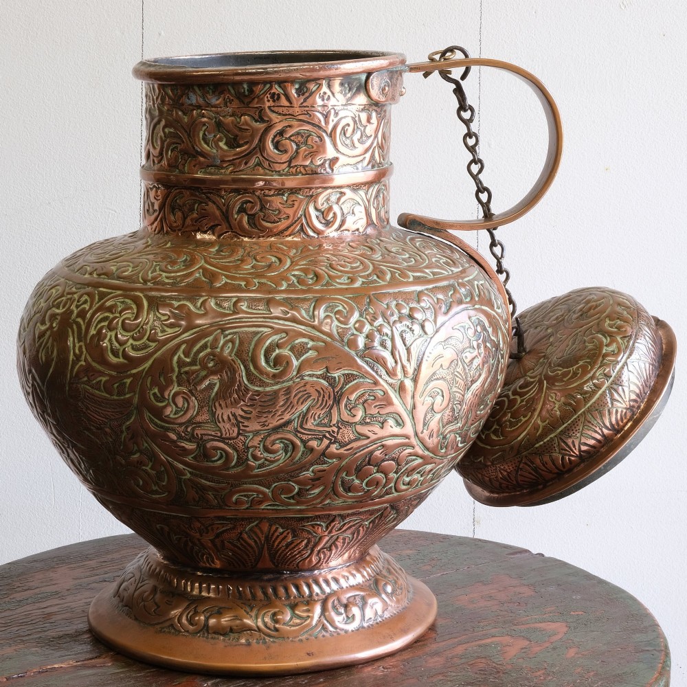 A large 18th-century copper jug featuring hand-chased foliate scrollwork and animal motifs, complete with a domed chained lid and curved handle. View II