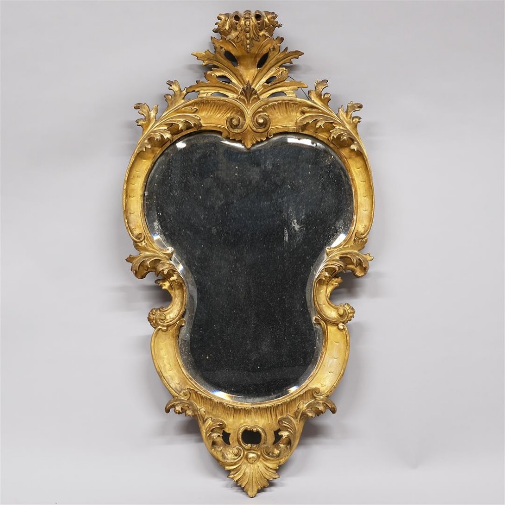 A 19th-century Venetian giltwood wall mirror featuring an ornately carved acanthus crest, C-scroll embellishments, and a contoured mirror plate.