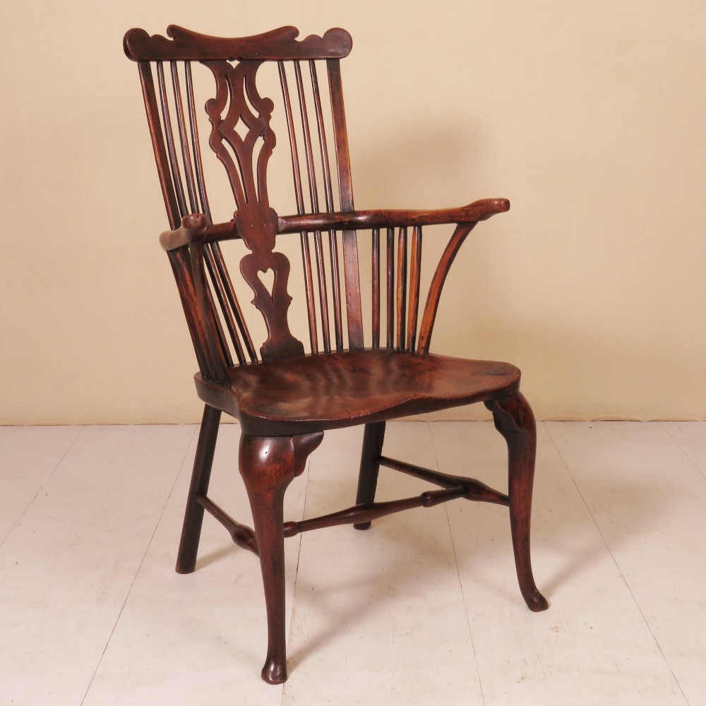 An 18th-century comb-back Windsor armchair in dark finished wood, featuring a pierced central splat, vertical spindles, curved armrests, and cabriole front legs.