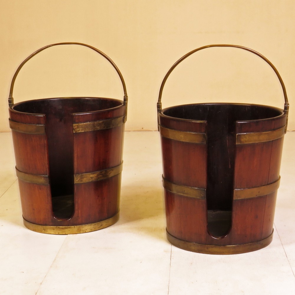 A pair of 18th-century mahogany plate buckets with brass binding hoops, overhead brass swing handles, and vertical front openings.