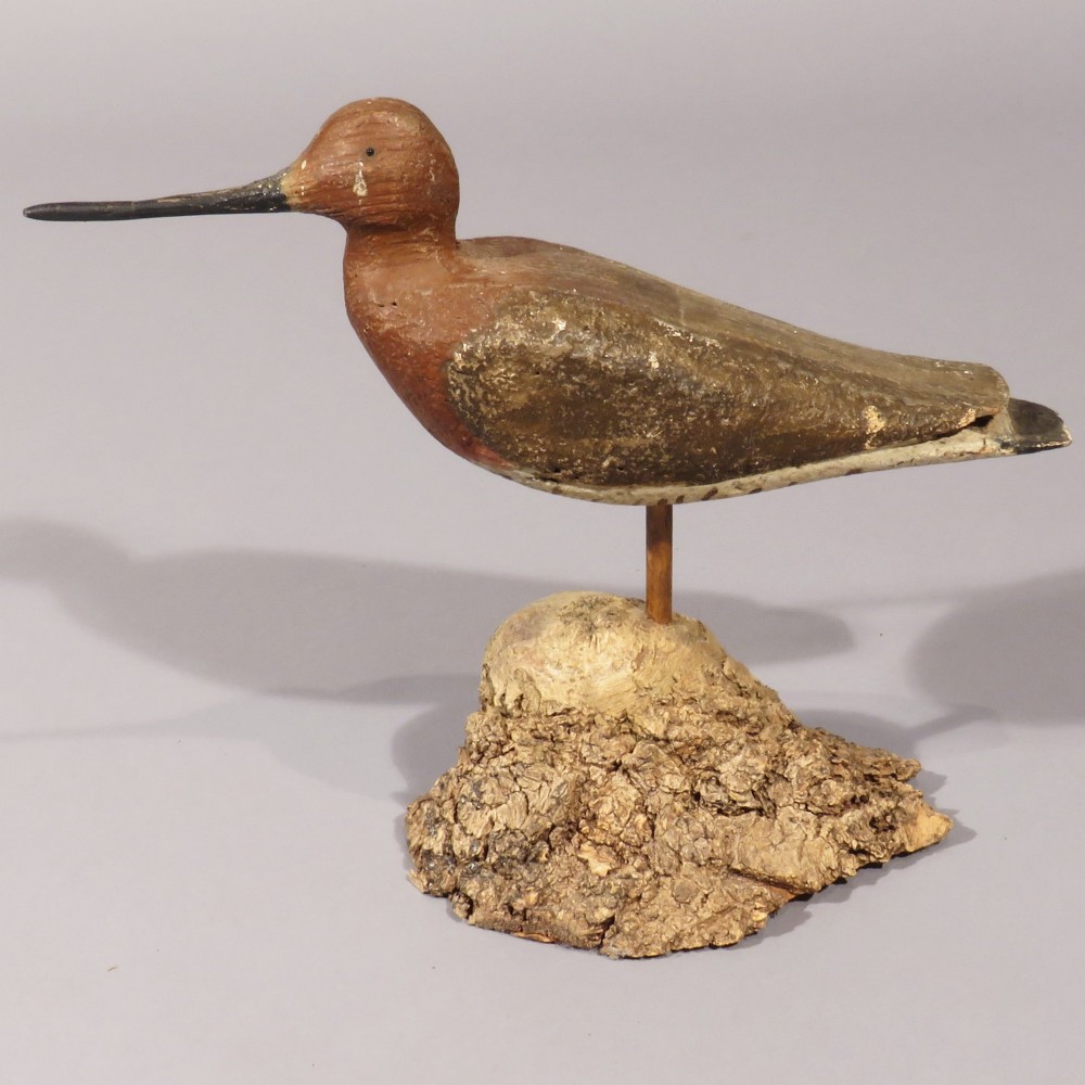 An antique hand-carved and painted wooden black-tailed godwit bird decoy with a long beak, mounted on a wooden rod set into a bark-covered base. View II