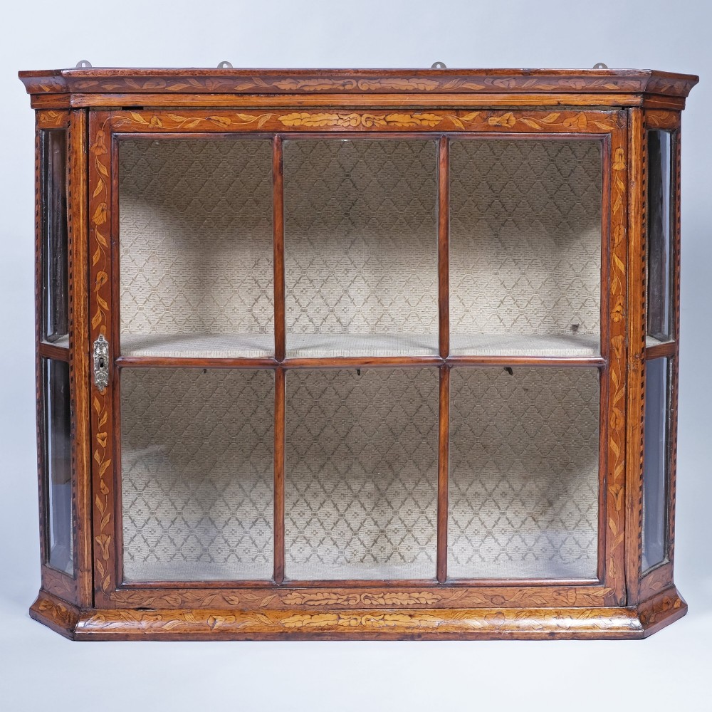 A late 18th-century warm brown wooden wall cabinet featuring floral marquetry inlay, glazed front and side panels, and a fabric-lined interior.