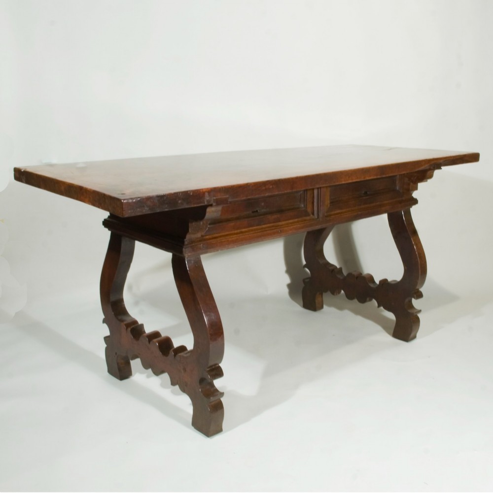 A 17th-century Spanish walnut table featuring curved lyre legs, decorative carved stretchers, and frieze drawers.