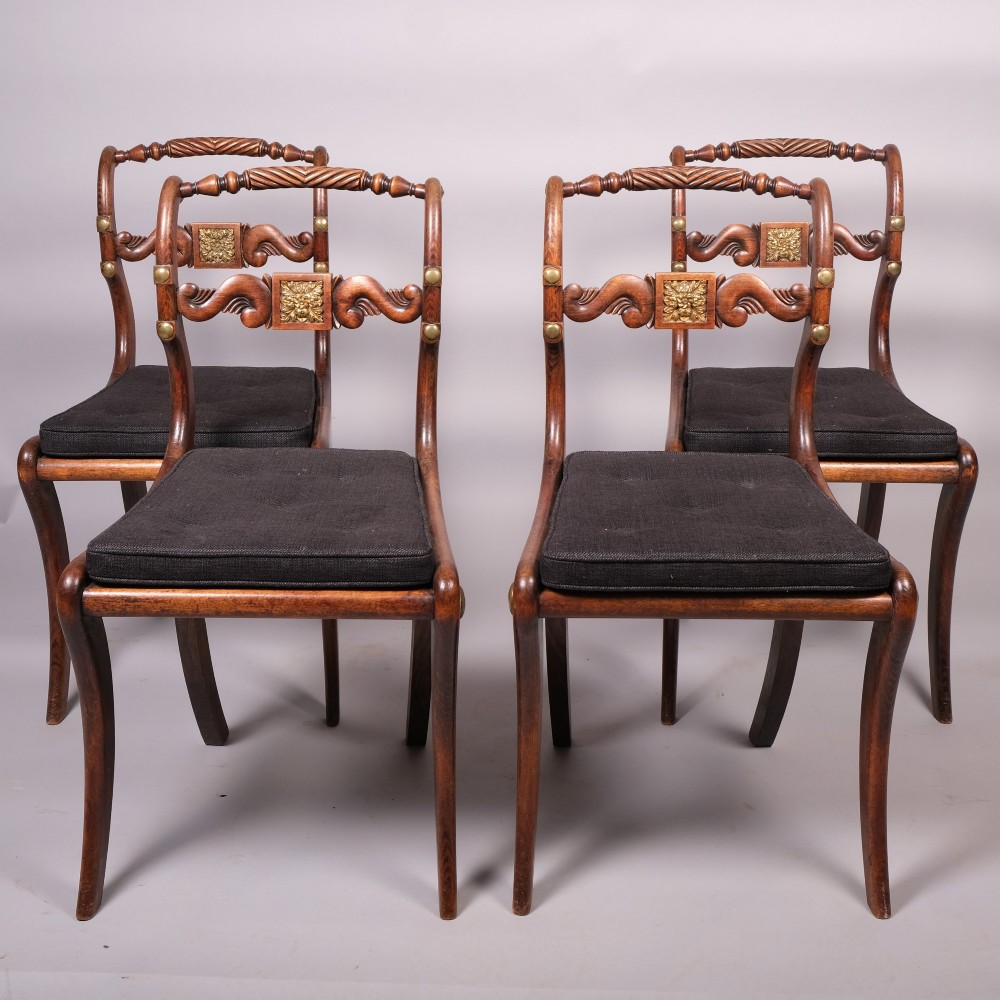 A set of four Regency dining chairs featuring simulated rosewood frames, carved rope twist top rails, brass mounts, and black upholstered seats.