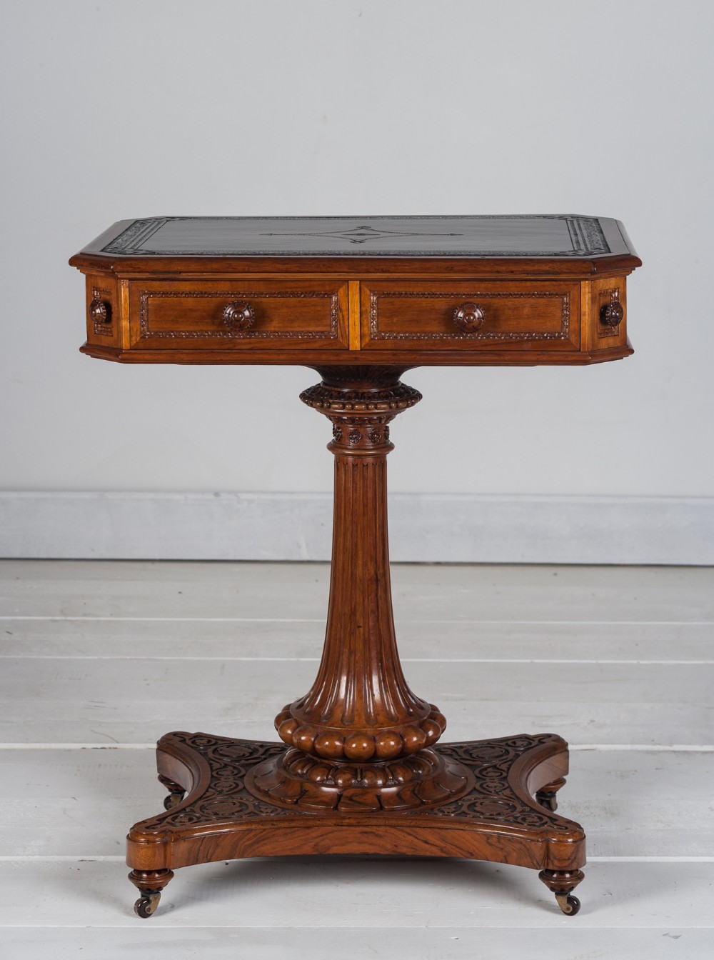 A nineteenth-century Regency mahogany reading table with a tooled leather inset top, carved drawer knobs, fluted pedestal column, and carved plinth base on castors.