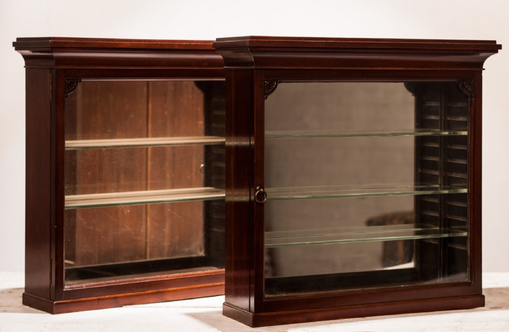A pair of dark mahogany display cabinets featuring glazed glass fronts, internal glass shelving, mirrored backings, and stepped top cornices.
