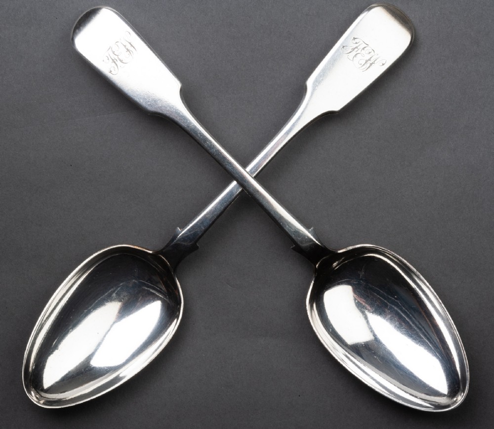 A pair of antique silver spoons featuring fiddle pattern handles engraved with cursive initials.