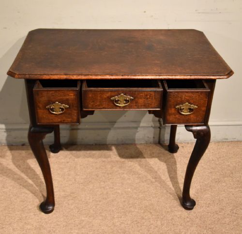 fig 1. A mid-18th century dark oak lowboy featuring three drawers with brass handles, a shaped lower apron, and cabriole legs with pad feet.