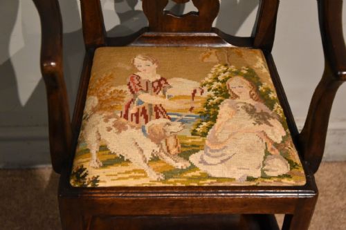 fig 1. An antique dark wood George III convertible highchair featuring a hand-carved pierced back splat, curved armrests, and a tapestry upholstered seat depicting figures in a landscape.