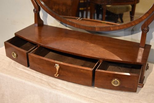 fig 1. A Regency mahogany bowfronted dressing mirror with an oval swivelling mirror plate, brass finial, and a three-drawer base with brass handles.