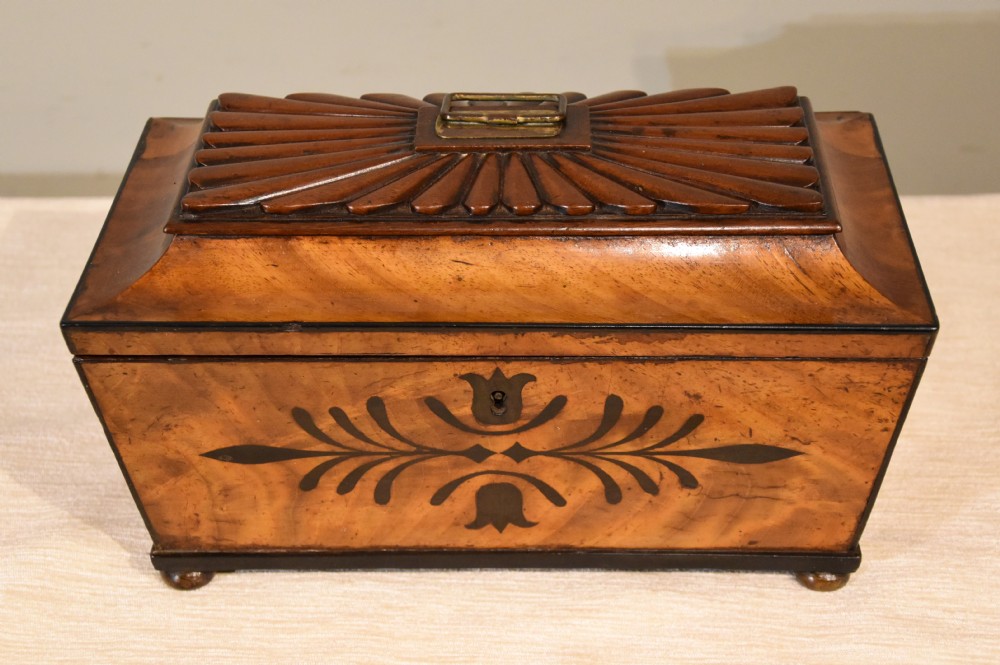 A 19th-century sarcophagus-shaped mahogany tea caddy with a carved fluted lid, ebony floral inlay on the front, and small feet.