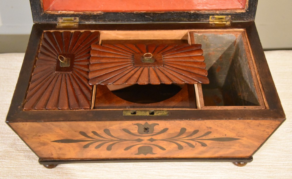 A 19th-century sarcophagus-shaped mahogany tea caddy with a carved fluted lid, ebony floral inlay on the front, and small feet. View VI