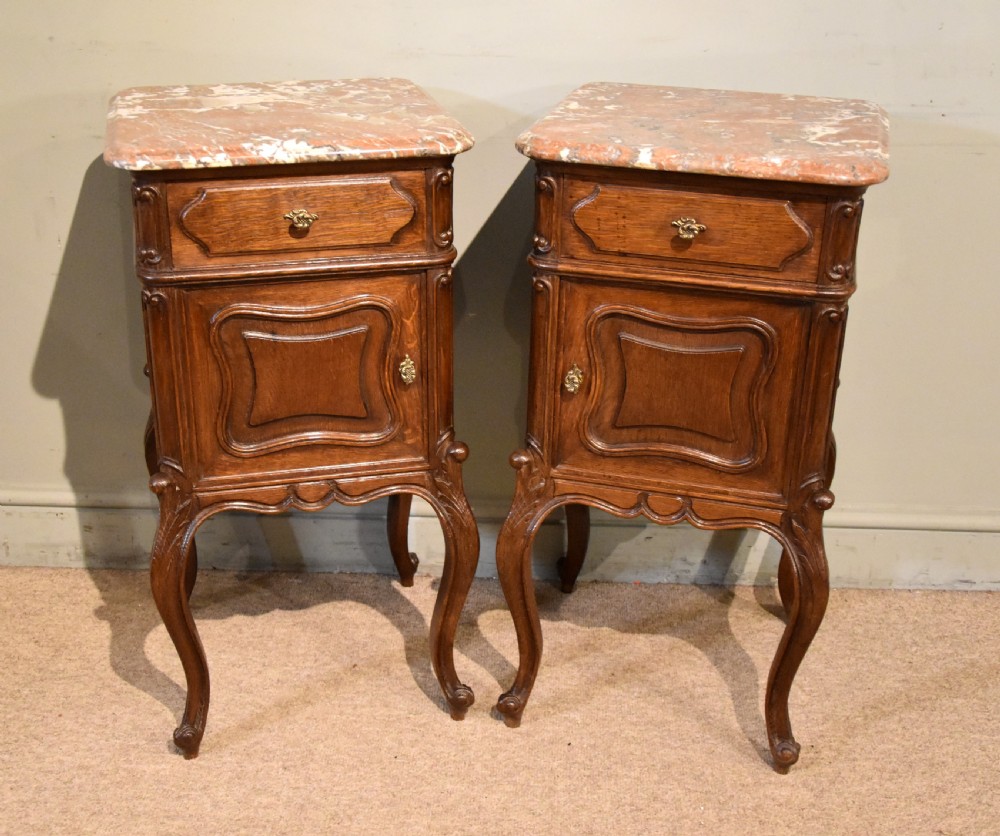 A pair of French carved oak bedside cabinets with variegated pink marble tops, single drawers, framed cupboard doors, and slender cabriole legs. View II