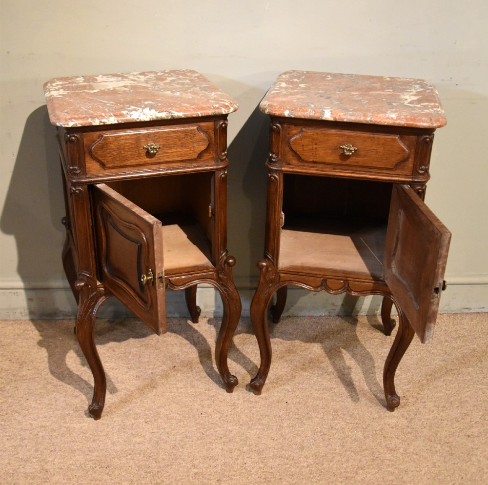A pair of French carved oak bedside cabinets with variegated pink marble tops, single drawers, framed cupboard doors, and slender cabriole legs. View IV