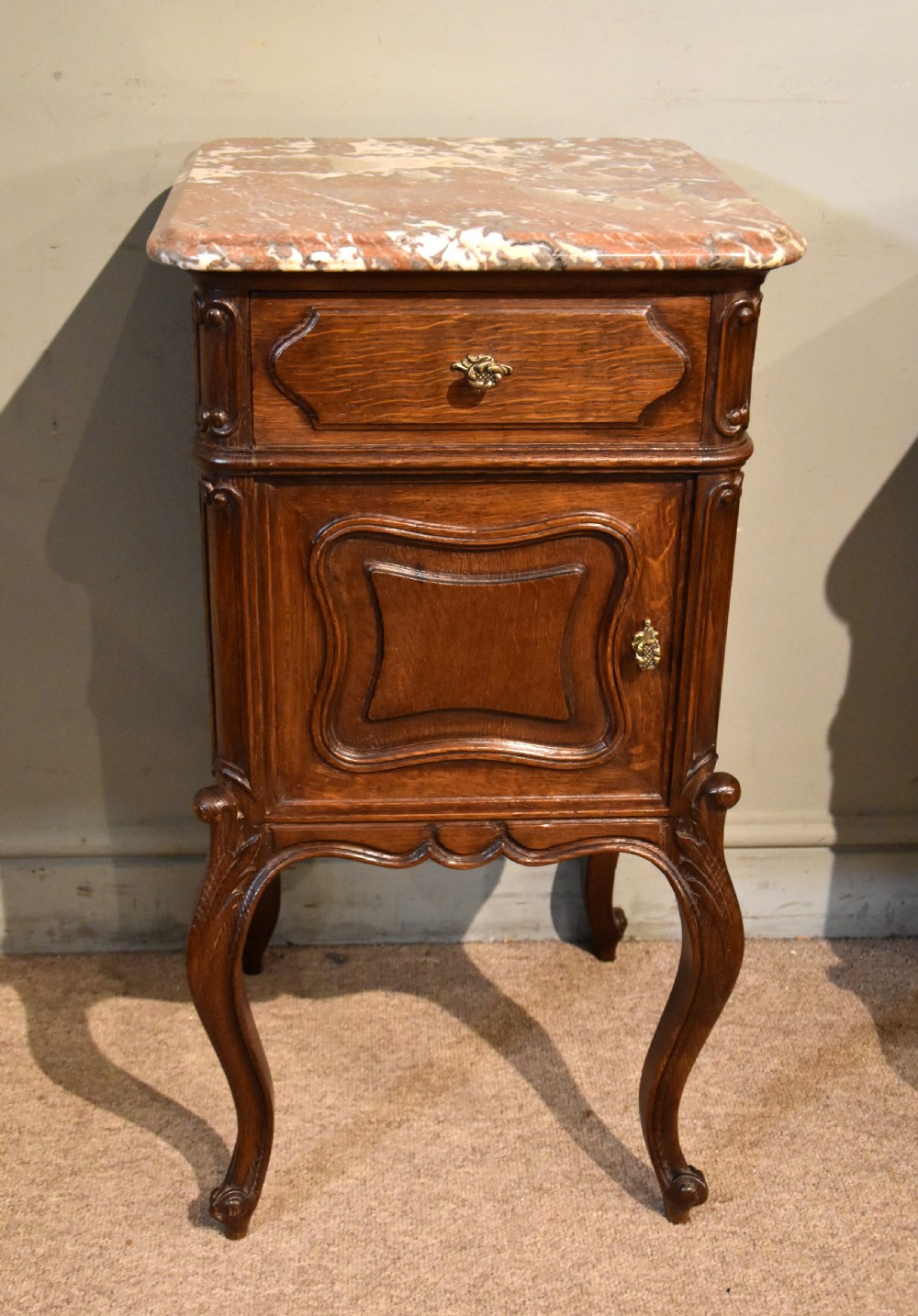 A pair of French carved oak bedside cabinets with variegated pink marble tops, single drawers, framed cupboard doors, and slender cabriole legs. View V