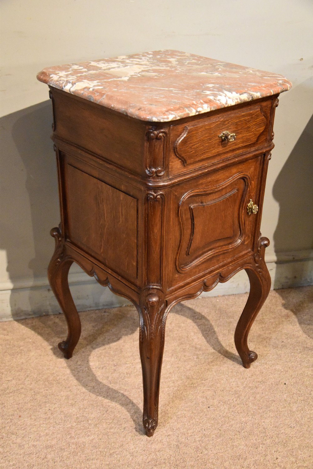 A pair of French carved oak bedside cabinets with variegated pink marble tops, single drawers, framed cupboard doors, and slender cabriole legs. View VI