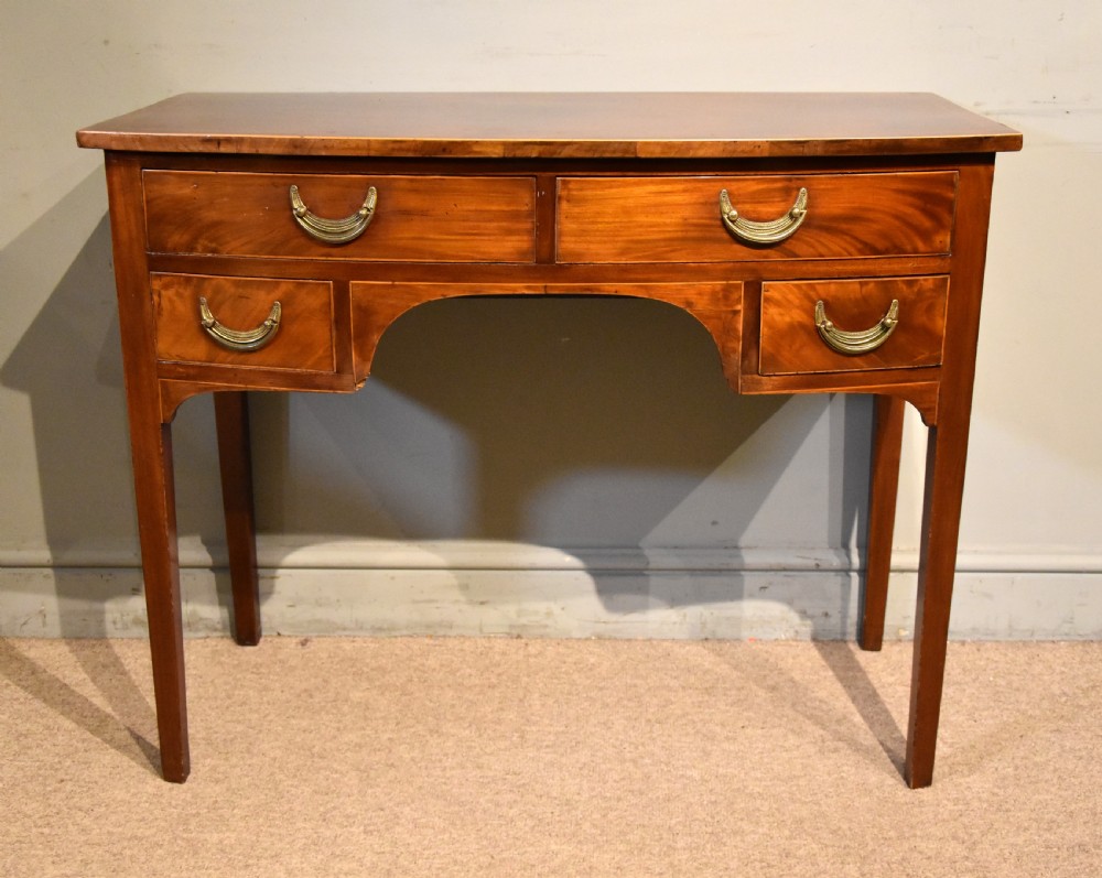 A 19th-century mahogany side table featuring four drawers with curved brass drop handles and an arched central apron set on four square tapering legs.