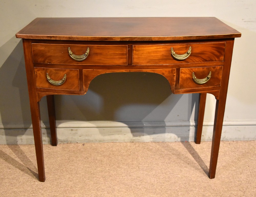 A 19th-century mahogany side table featuring four drawers with curved brass drop handles and an arched central apron set on four square tapering legs. View II