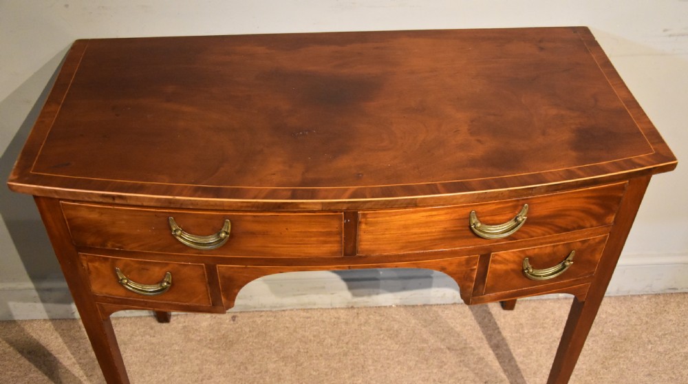 A 19th-century mahogany side table featuring four drawers with curved brass drop handles and an arched central apron set on four square tapering legs. View IV