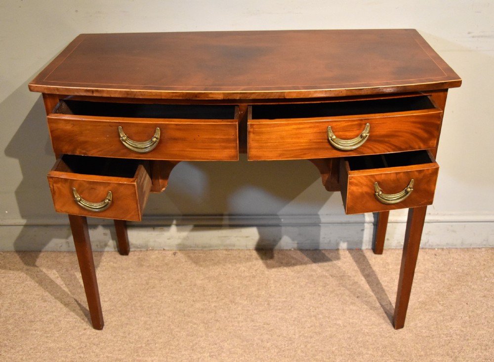 A 19th-century mahogany side table featuring four drawers with curved brass drop handles and an arched central apron set on four square tapering legs. View V