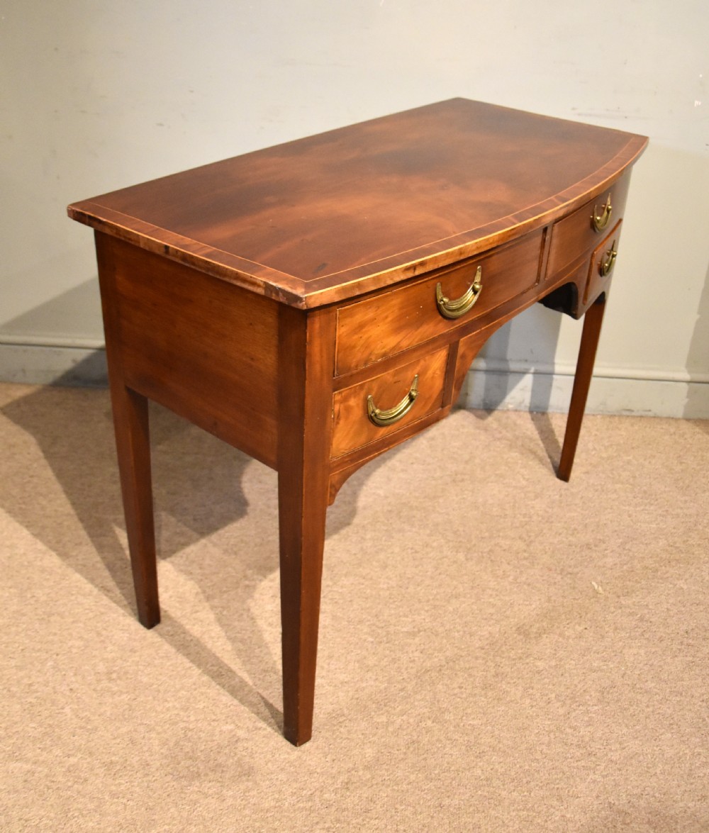 A 19th-century mahogany side table featuring four drawers with curved brass drop handles and an arched central apron set on four square tapering legs. View VI