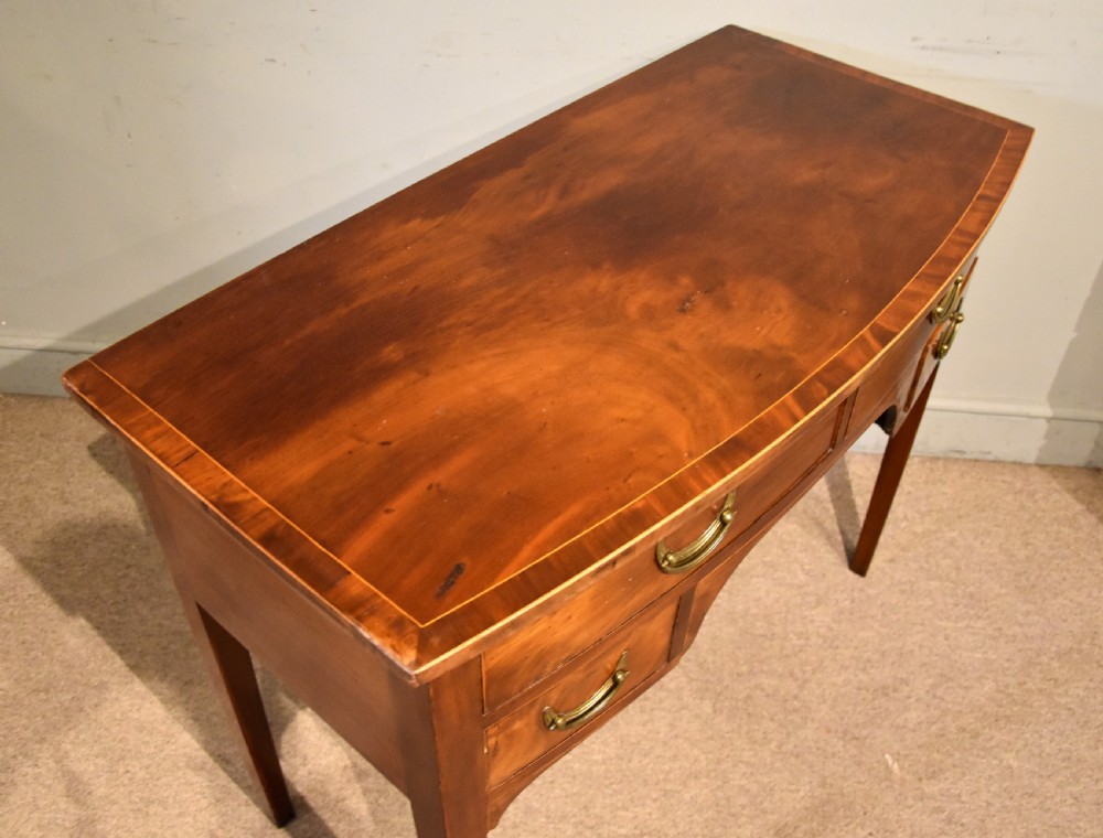 A 19th-century mahogany side table featuring four drawers with curved brass drop handles and an arched central apron set on four square tapering legs. View VII