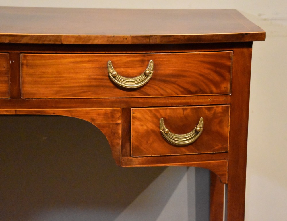 A 19th-century mahogany side table featuring four drawers with curved brass drop handles and an arched central apron set on four square tapering legs. View VIII
