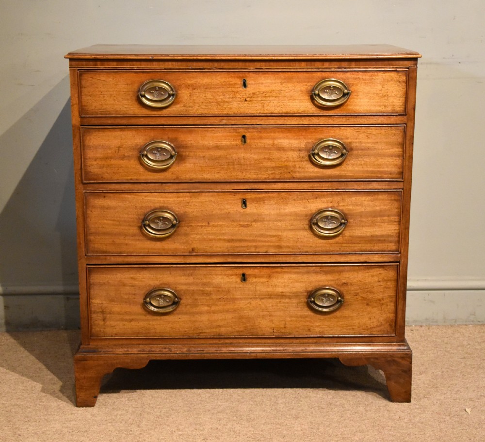 A George III mahogany chest of drawers featuring four graduated drawers with oval brass plate handles and shaped bracket feet. View II