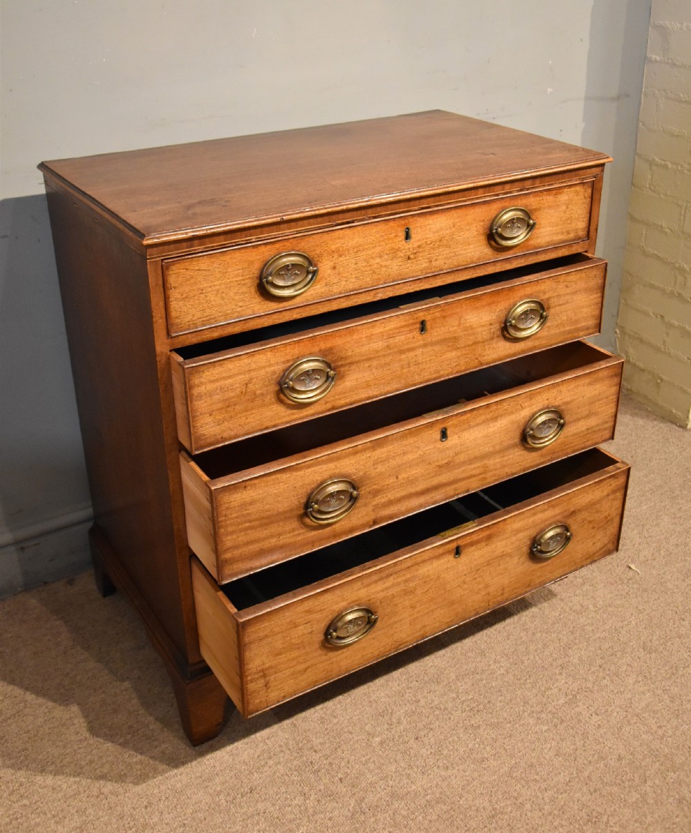 A George III mahogany chest of drawers featuring four graduated drawers with oval brass plate handles and shaped bracket feet. View IV