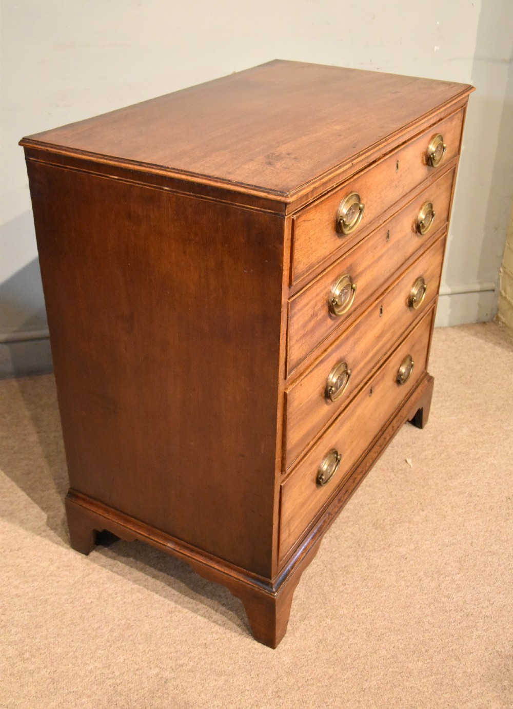 A George III mahogany chest of drawers featuring four graduated drawers with oval brass plate handles and shaped bracket feet. View VII