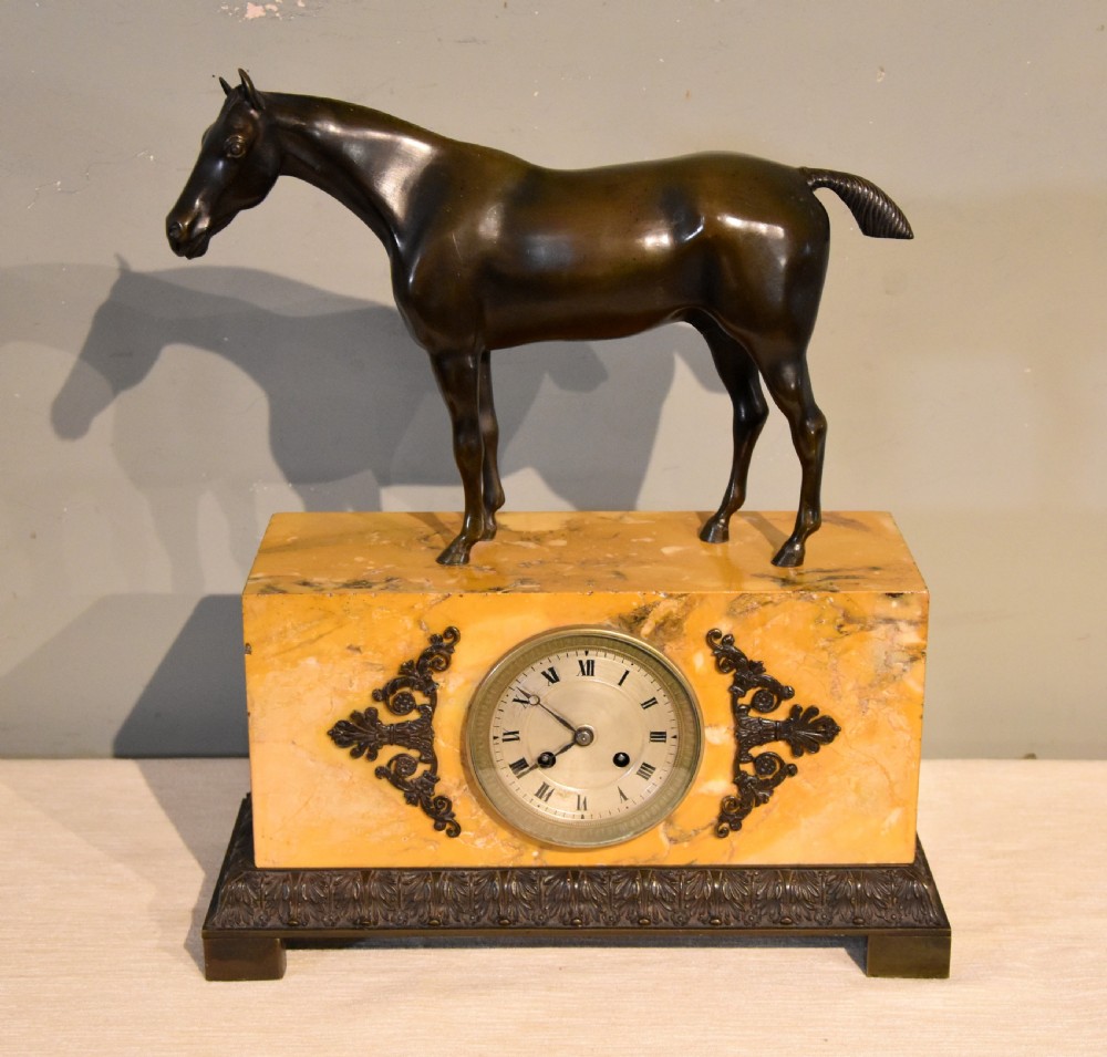 An antique mantel clock featuring a patinated bronze stallion standing atop a rectangular yellow Siena marble base with decorative scroll appliques and a circular dial with Roman numerals. View II