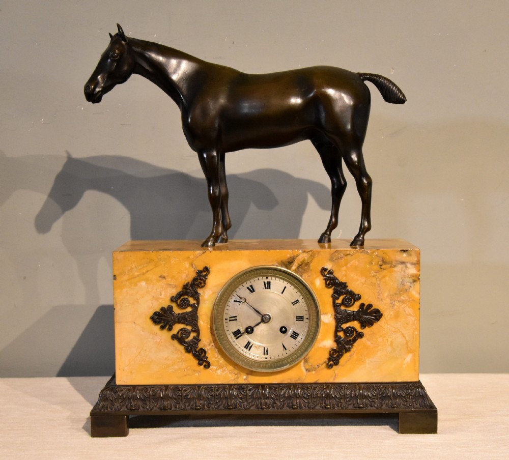 An antique mantel clock featuring a patinated bronze stallion standing atop a rectangular yellow Siena marble base with decorative scroll appliques and a circular dial with Roman numerals. View III