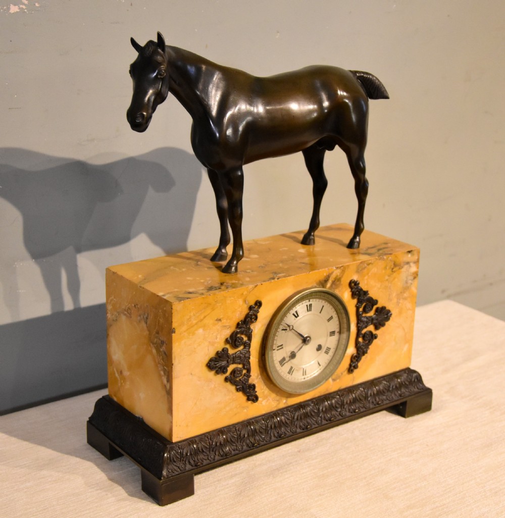 An antique mantel clock featuring a patinated bronze stallion standing atop a rectangular yellow Siena marble base with decorative scroll appliques and a circular dial with Roman numerals. View IV