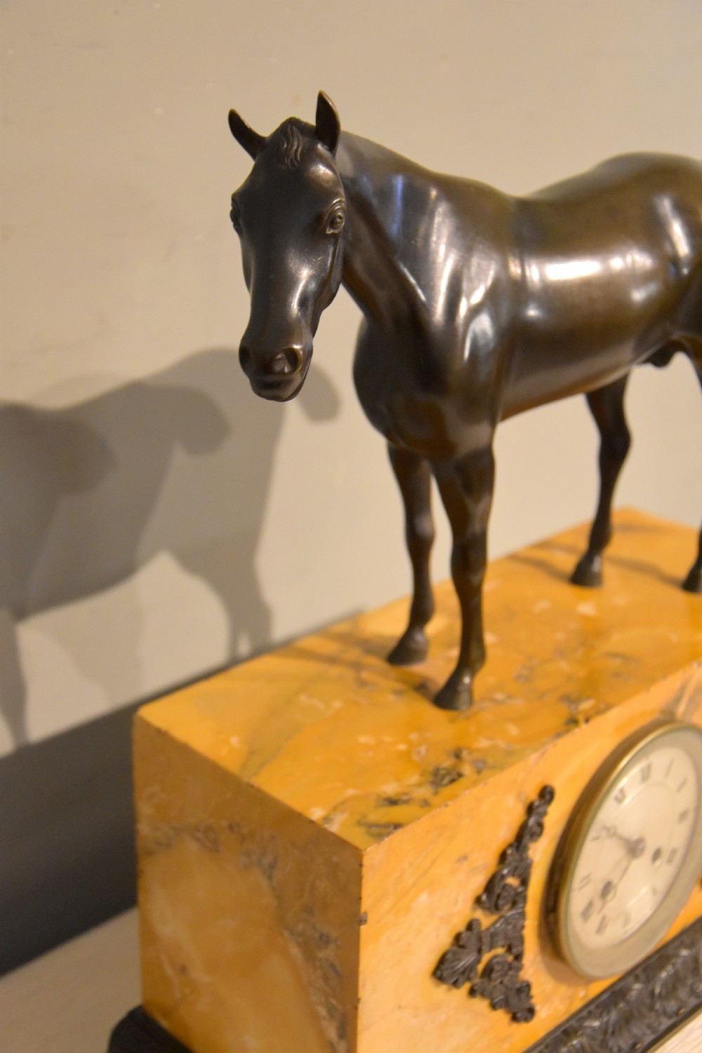 An antique mantel clock featuring a patinated bronze stallion standing atop a rectangular yellow Siena marble base with decorative scroll appliques and a circular dial with Roman numerals. View V