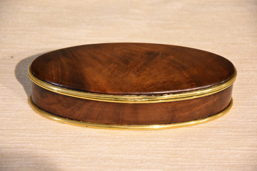 An eighteenth-century oval walnut table snuff box with figured grain and polished brass rim bindings.