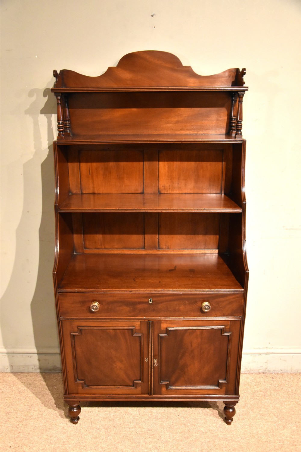 A Regency period mahogany waterfall bookcase featuring graduated open shelves, a single drawer, two lower cabinet doors, and turned feet. View III