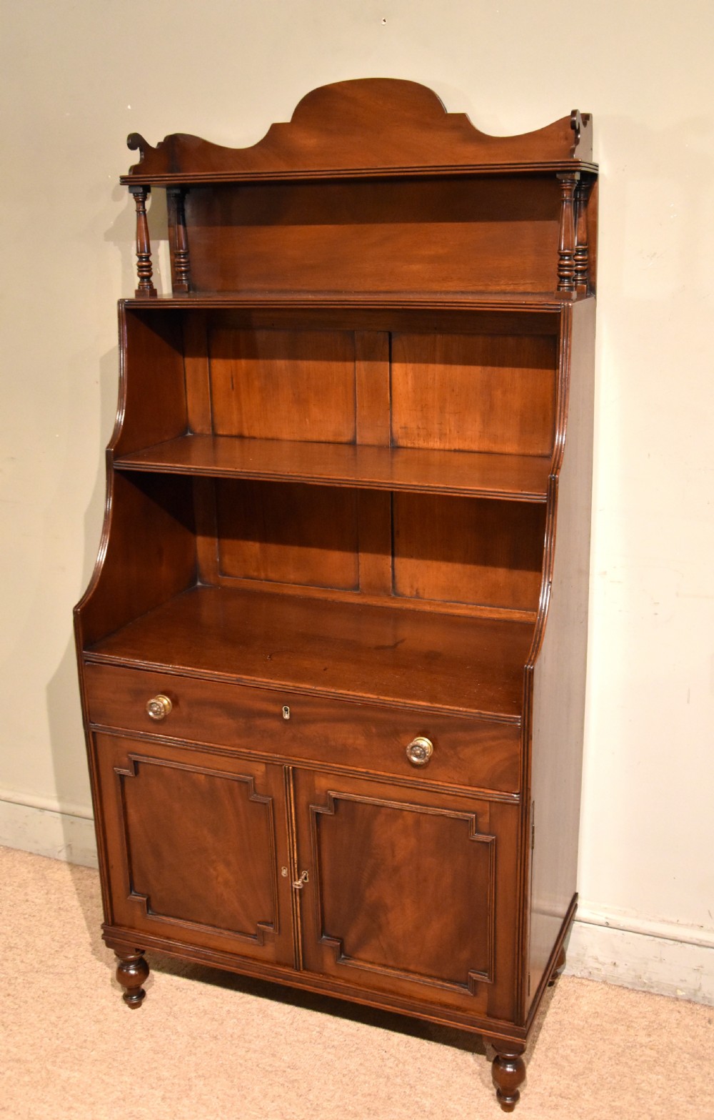 A Regency period mahogany waterfall bookcase featuring graduated open shelves, a single drawer, two lower cabinet doors, and turned feet. View IV