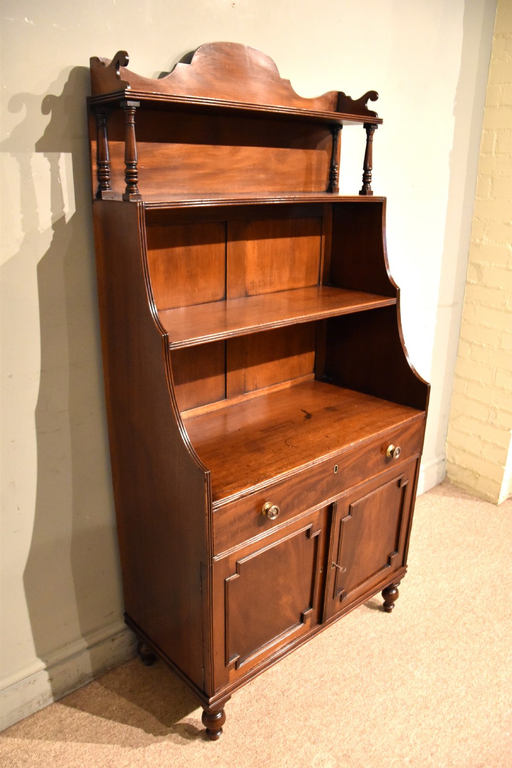 A Regency period mahogany waterfall bookcase featuring graduated open shelves, a single drawer, two lower cabinet doors, and turned feet. View V