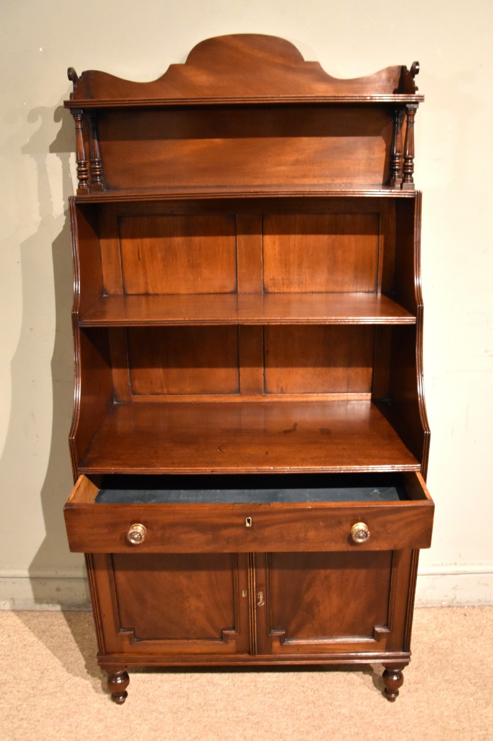 A Regency period mahogany waterfall bookcase featuring graduated open shelves, a single drawer, two lower cabinet doors, and turned feet. View VI